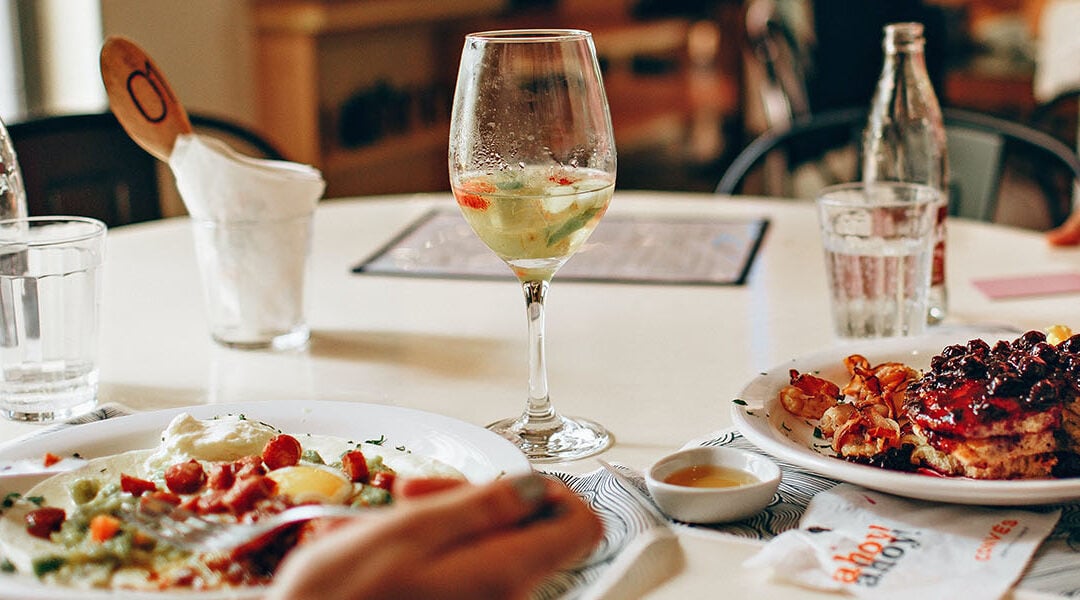 Table with two plates of food, wine glass, and soda bottle with glass.