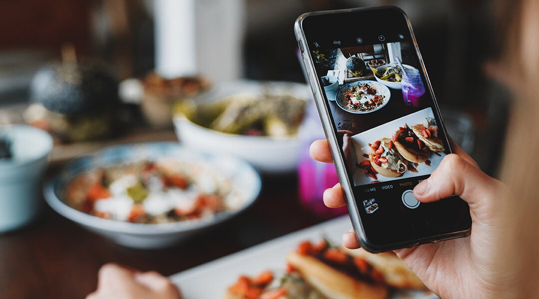 A hand, holding a phone over table of food, preparing to take a picture of a dish.