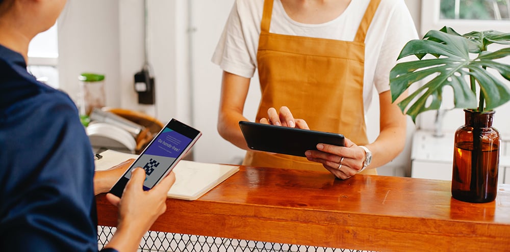 A customer checks out of a business with a cashier in a tan apron.