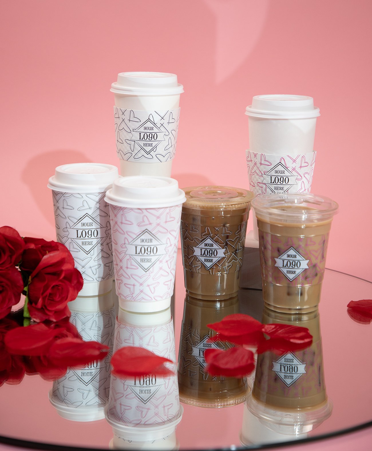 Valentine's Day themed cups on a mirror with rose petals and pink backdrop.