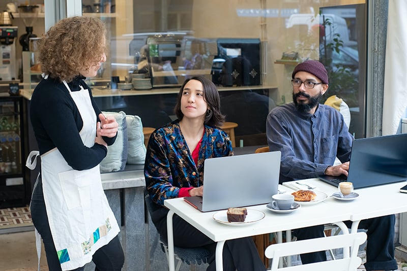 Two people sitting at a table, listening to a waitress.