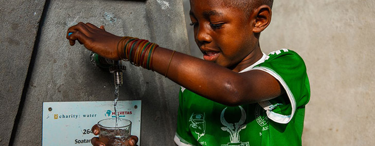 A young child pours clean water into a glass cup.