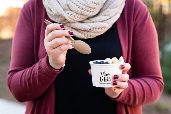 Your Brand Cafe A hand begins to dip a spoon into a custom printed ice cream cup topped with fruit.