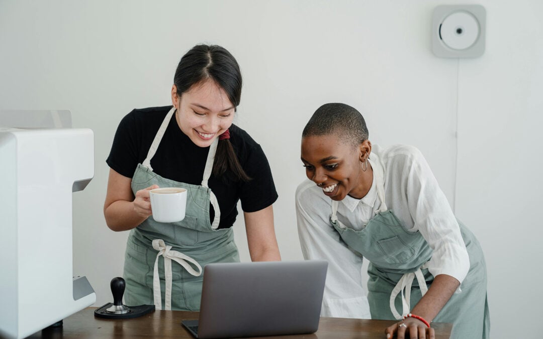 Two people in aprons look over a laptop on a desk.