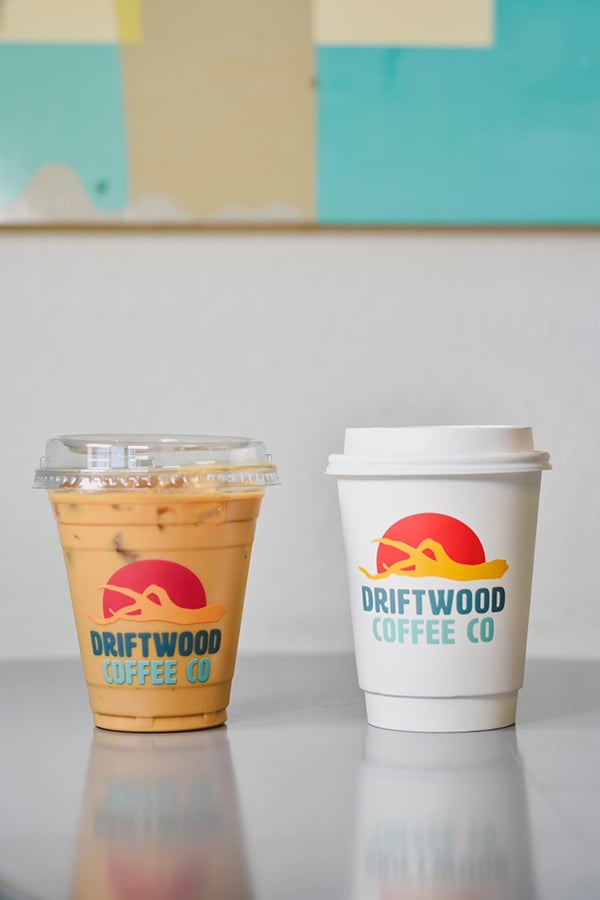 A custom printed logo on a plastic cold cup with iced coffee and an insulated hot cup with a white lid.