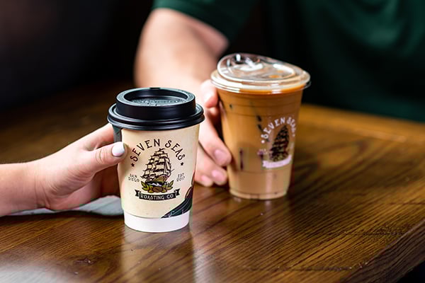 Hands hold a custom printed plastic cup and an insulated hot cup.