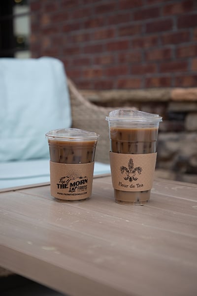 Two plastic cold cups wrapped in custom printed kraft sleeves