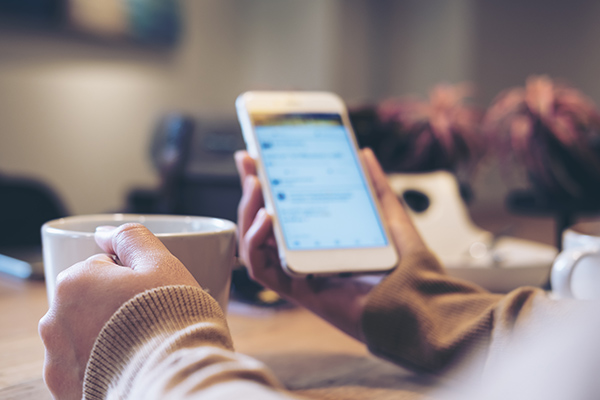 A woman's hands holding white coffee cup and mobile phone while using social media in modern loft cafe