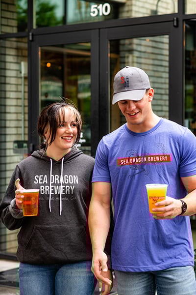 Two people holding beers walk out of a brewery