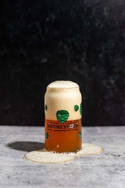 A beer can glass overflows with beer.