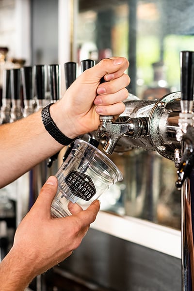 Two hands pour beer from a tap into a custom printed plastic cup