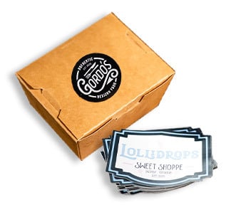 A paper to-go box with a label and a stack of custom printed vinyl stickers